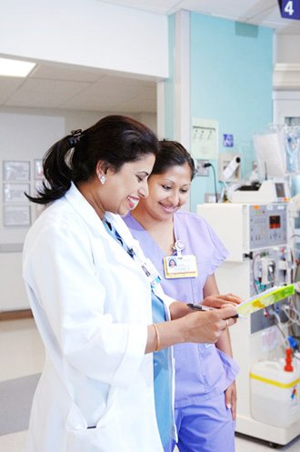 Two clinicians reviewing settings on a dialysis machine